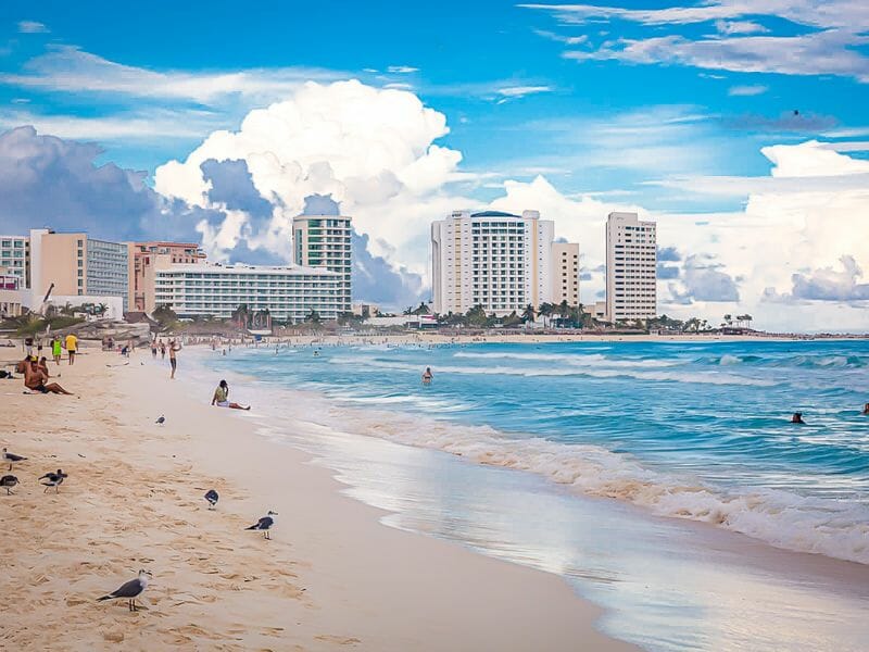 People on cancun beach clouds in the background behind the buldings