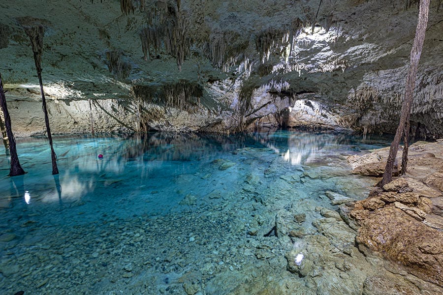 A stunning underground cenote with clear turquoise water and limestone stalactites creates a breathtaking natural environment for exploration and adventure.
