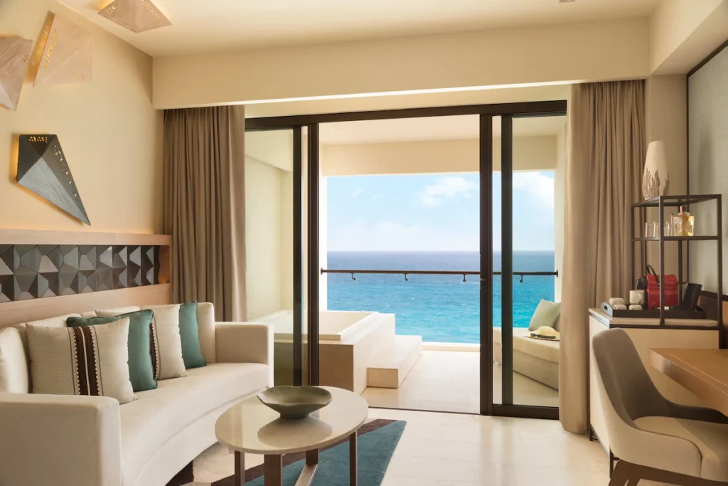 room with couch, table, desk and mini bar and a terrace overlooking the water