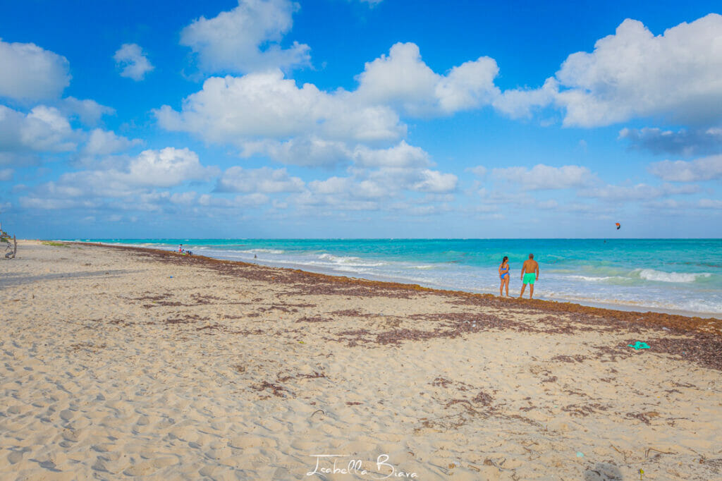 Couple walking on the beach in Isla Blanca while a kiter is flying in the background