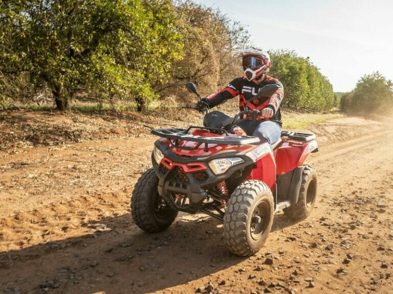 A man in complete gear on a red ATV on a sunny day.