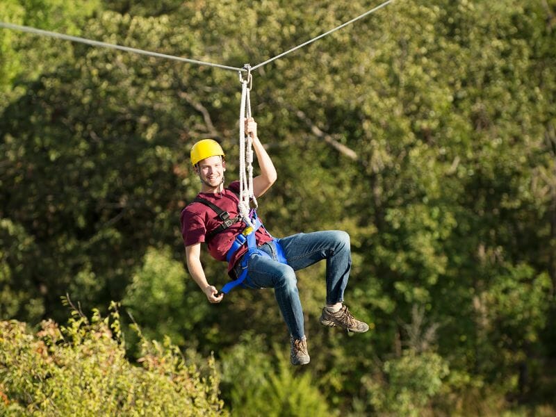 A man in a yellow helmet ziplined on a sunny day. 