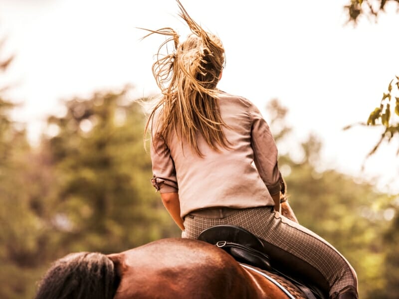 rear view of woman practicing horseback riding outdoors