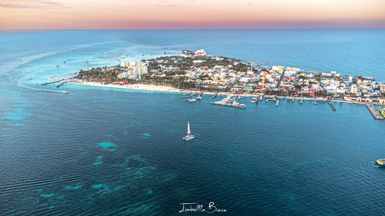 Aerial view of Isla Mujeres, a small island near Cancun. The colorful buildings, marina with boats, white sandy beaches, and turquoise waters create a stunning landscape where the horizon blends the sea with the sky.
