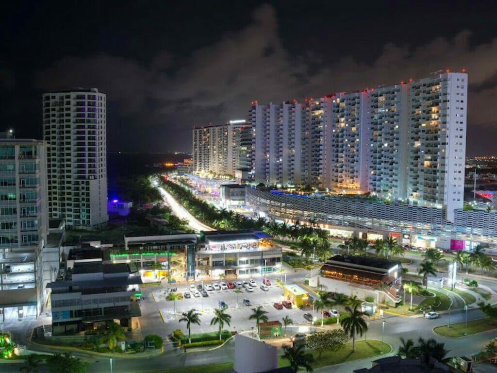 View of Plaza Las Americas Cancun and nearby buildings at night.