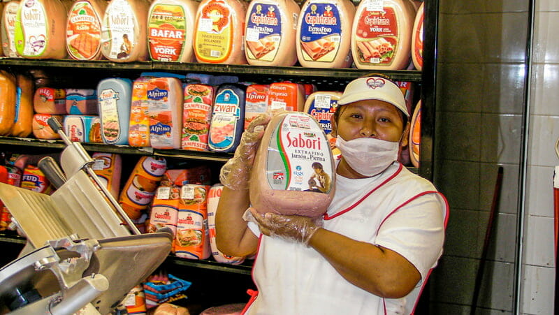 View of the cold cuts section with an employee holding the meat at Walmart in Cancun