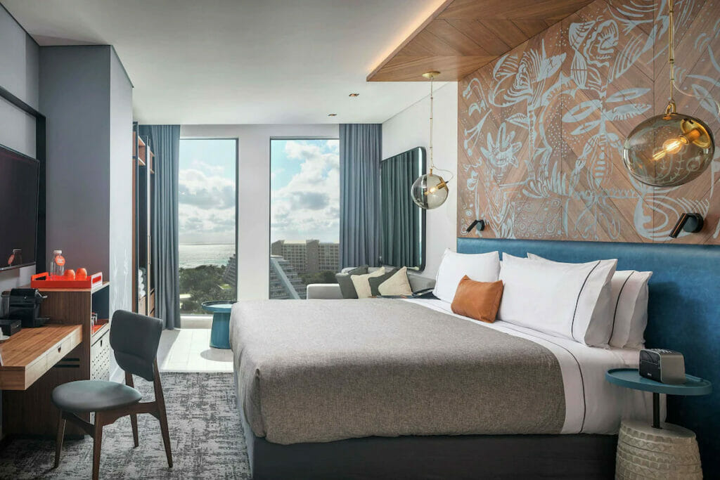 A hotel room with a bed, tables and chairs and huge window.