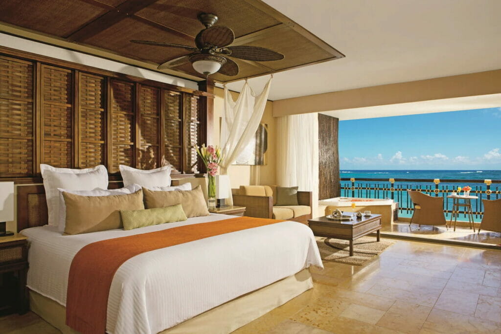 A hotel in Cancun with a cozy bed, tables and chairs and a balcony.