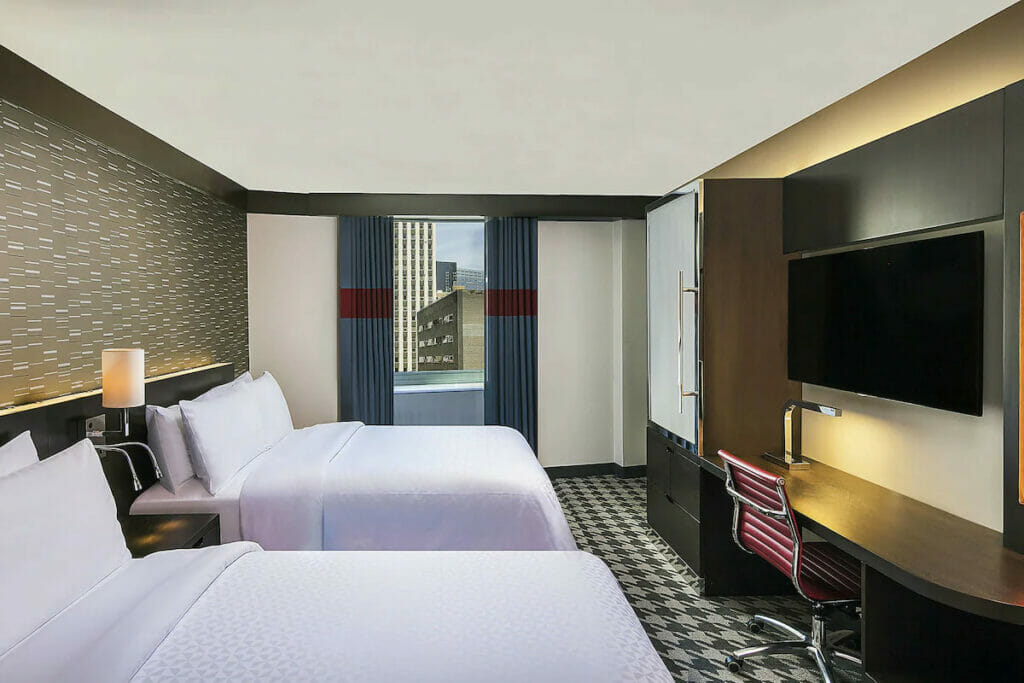 A hotel in Cancun with a couple of beds, flat screen TV and a window.
