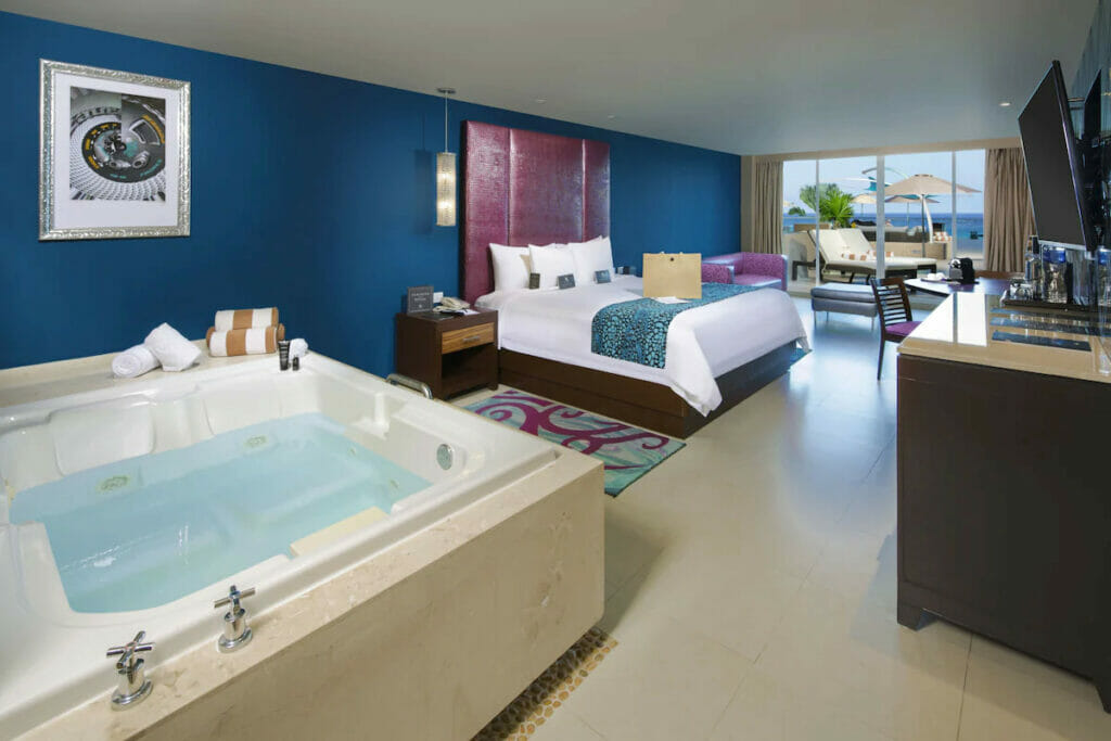 A luxury hotel in Cancun with a cozy bed near the jacuzzi, tables and chairs and balcony.