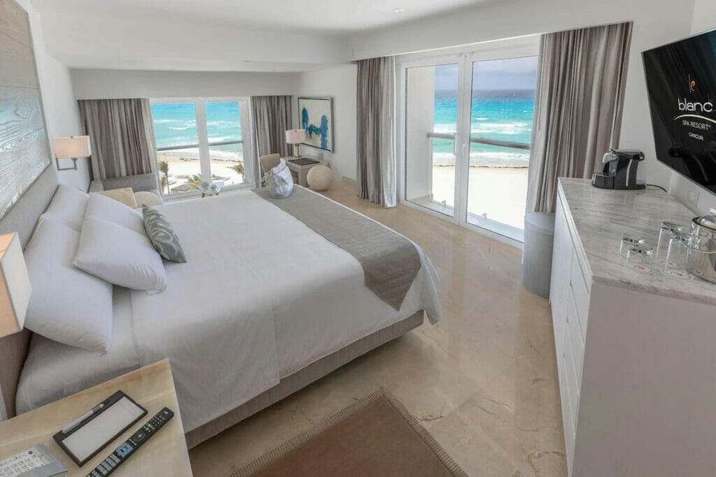 An all white room in a hotel in Cancun with bed and view of the sea from the balcony.