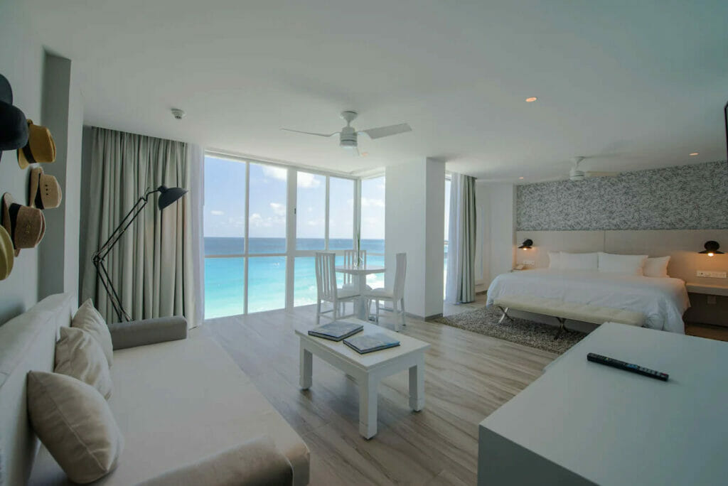 A spacious bedroom with a cozy bed, tables and chairs and a ceiling-to-floor window.