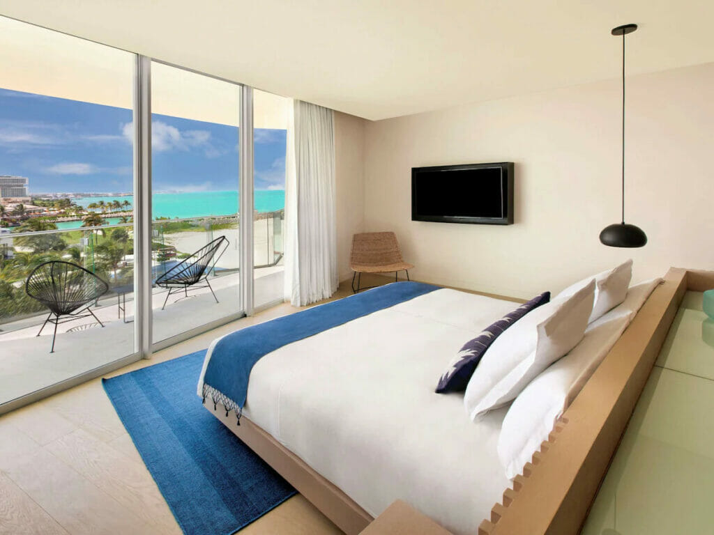 A room with a cozy bed with a balcony and view of the beach.