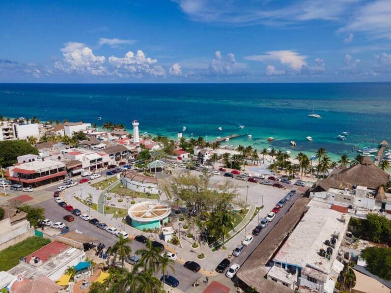 Aerial view of a coastal town with a central park, surrounding buildings, and a turquoise ocean in the background.