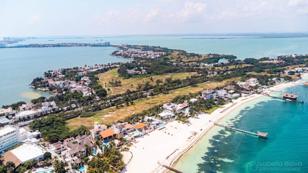 Aerial view of a beachside town with turquoise water, rows of palm trees, and homes lining the shore.