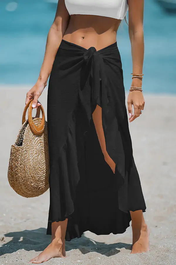Woman in black skirt on beach with straw bag.