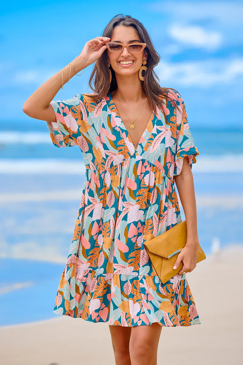 Woman in colorful dress, smiling at the beach.