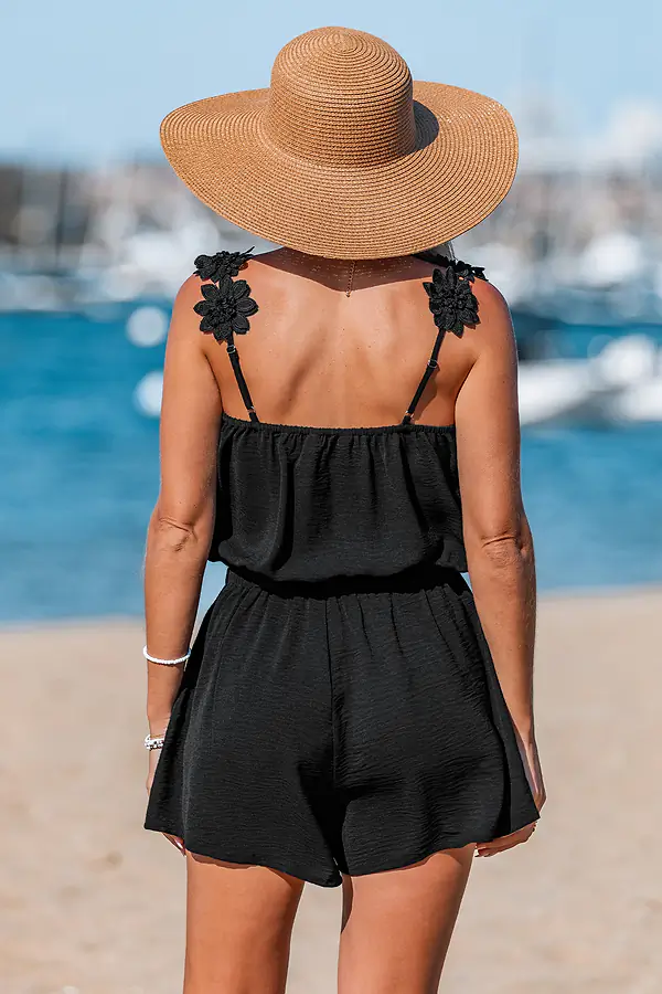 Woman in black romper and straw hat at beach.