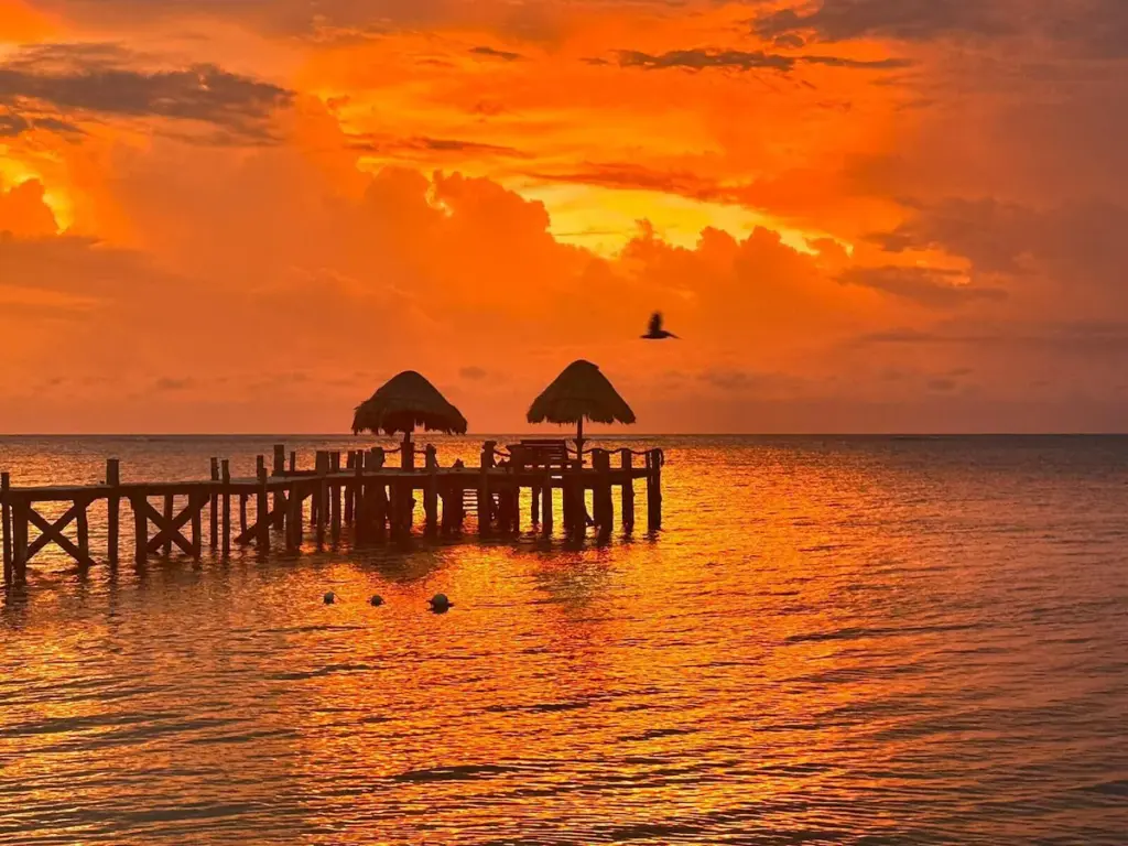 Sunset over ocean pier with orange glow.